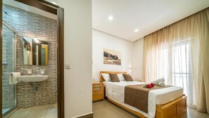A hotel room with a bed, a bedside table, a nightstand, a mirror, a sink, and a window with curtains. -  Apartment with balcony and sea views, fully A/c (Marsalforn)