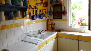 Une cuisine aux carreaux jaunes et blancs, avec un fourneau, un évier et divers ustensiles de cuisine et casseroles accrochés au mur.