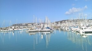 Un port de plaisance où de nombreux bateaux sont amarrés, l’eau est calme et le ciel est d’un bleu limpide.
