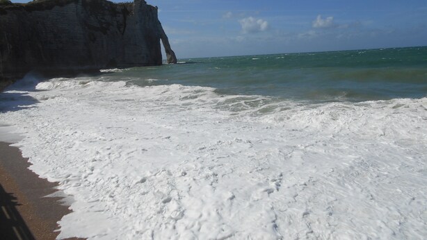 Une plage aux vagues d’écume blanche, une grande falaise et un ciel bleu azur.