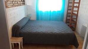 A small, cozy room with a single bed, a small table, a lamp, and a wooden ladder against the wall.