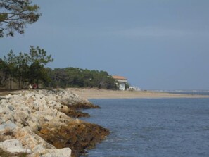 A coastal property with a rocky shoreline, a building with a red roof, and a beach in the background.