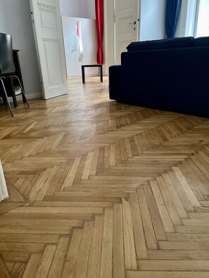 A room with a herringbone wooden floor, a blue sofa, and a white wardrobe.