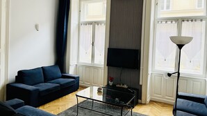 En moderne stue med en mørkeblå sofa, et glasbord og et fladskærms-tv monteret på væggen.
