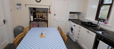 A kitchen with a blue polka dot tablecloth, white cabinets, a microwave, a washing machine, and a clock on the wall.