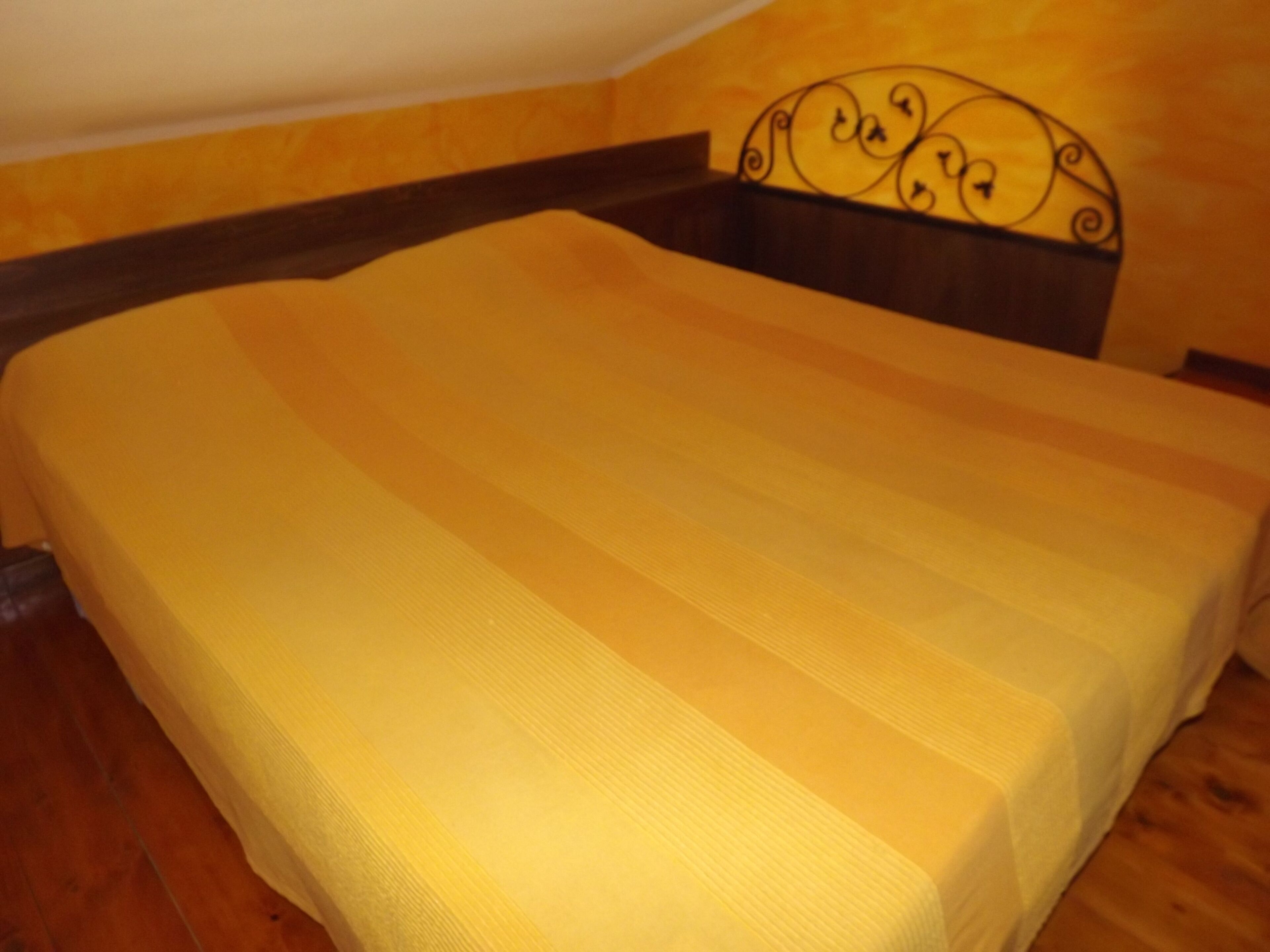 Un lit avec une couvre-lit à rayures jaunes, une tête de lit en bois ornée d’un élément décoratif, et un plancher en bois.