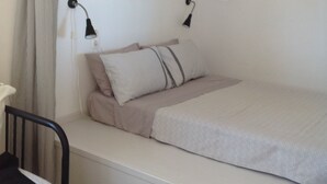 En enkeltseng med hvid madras og himmelseng, et sengebord, en lampe og en stol med sort ramme.