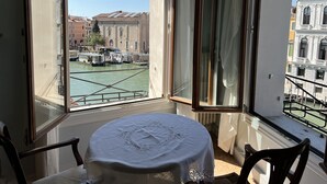 A room with a large window overlooking a canal with boats, featuring a round table with a white tablecloth and chairs.