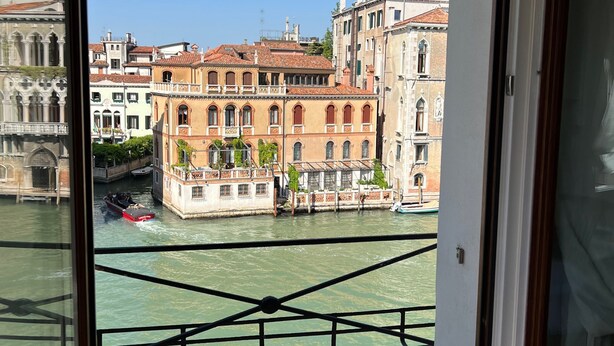 A view from a window overlooking a canal with historic buildings, a boat, and a clear sky.
