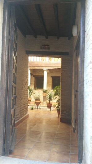 An interior corridor with a tiled floor, brick walls, and a wooden ceiling. There are potted plants and a window with bars. - Spacious Attic with Terrace Alhambra Full Views (Granada)