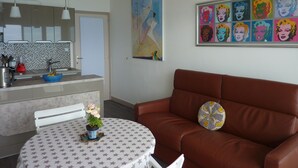 A modern kitchen with a sink, a dining table with a star-patterned tablecloth, a brown leather sofa, and a colorful pop art mural on the wall. - Magnificent apartment T3 sea view 180 degrees, Sea at 20 meters (Le Lavandou)