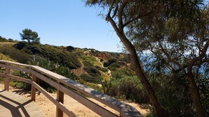 A wooden bridge with a metal railing, leading to a hilly landscape with sparse vegetation and a clear sky. - Lovely Apartment, Ponta da Piedade Natural Reserve, Camilo Beach, Dona Ana Beach (Lagos)