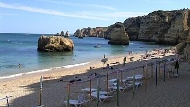 A beach with clear blue water, rocky formations, and sun loungers along the shore. - Lovely Apartment, Ponta da Piedade Natural Reserve, Camilo Beach, Dona Ana Beach (Lagos)