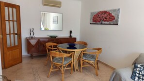 Uma sala de jantar com uma mesa redonda e cadeiras de vime, um armário de madeira e um espelho na parede.