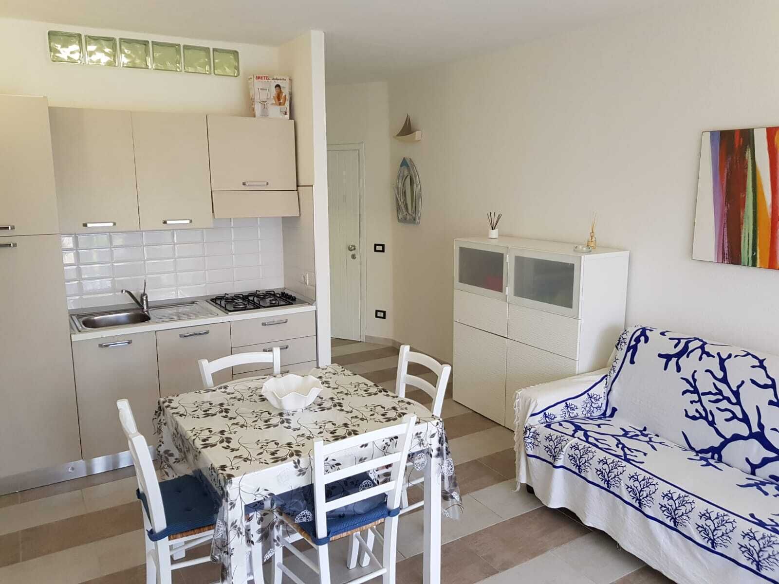 A compact kitchen with a dining area, white cabinets, and a sofa with a blue and white pattern.