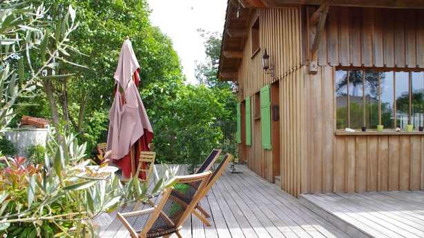 A wooden deck with outdoor furniture, including a table and chairs, and a wooden building with a window and a door. - Cap Ferret charming wooden villa (Lège-Cap-Ferret)