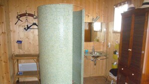 A bathroom with a tiled shower, a glass sink, a wooden door, and a shelf with toiletries. - Cap Ferret charming wooden villa (Lège-Cap-Ferret)