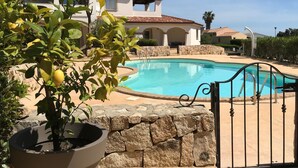 Une piscine bordée d’un muret en pierre et dotée d’un portail en métal, entourée d’un espace aménagé avec des plantes en pot.