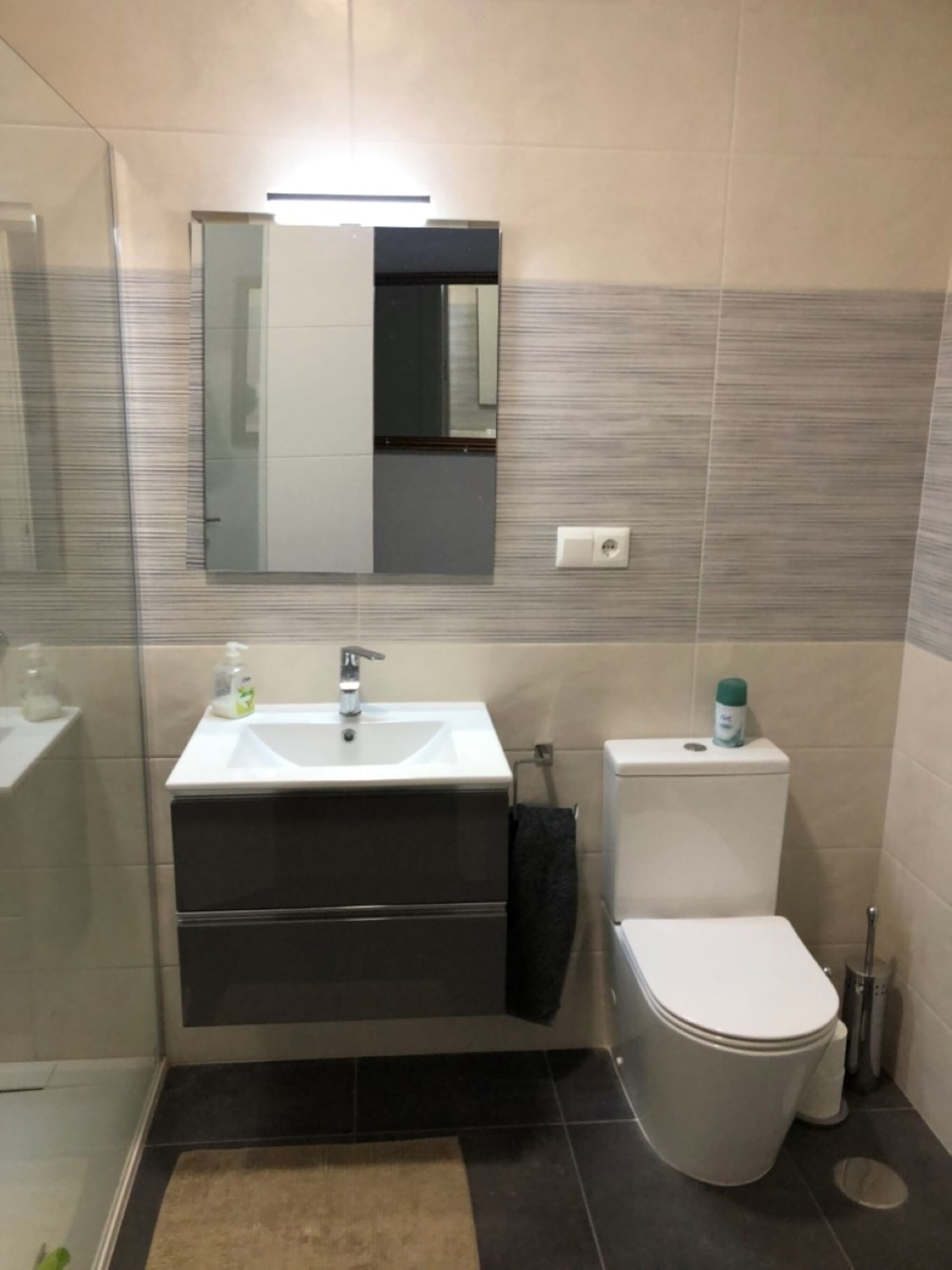 Une salle de bain avec un lavabo blanc, un miroir, des toilettes et un espace douche.