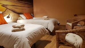 Ett hotellrum med två sängar, en stor tavla som föreställer en solnedgång, en flätad stol och ett fönster med persienner.