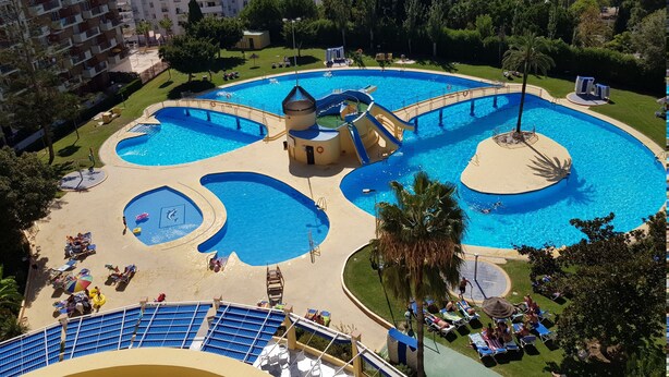 En stor utomhuspool med flera avdelningar, inklusive en central vattenrutschkana och en liten, rund pool.