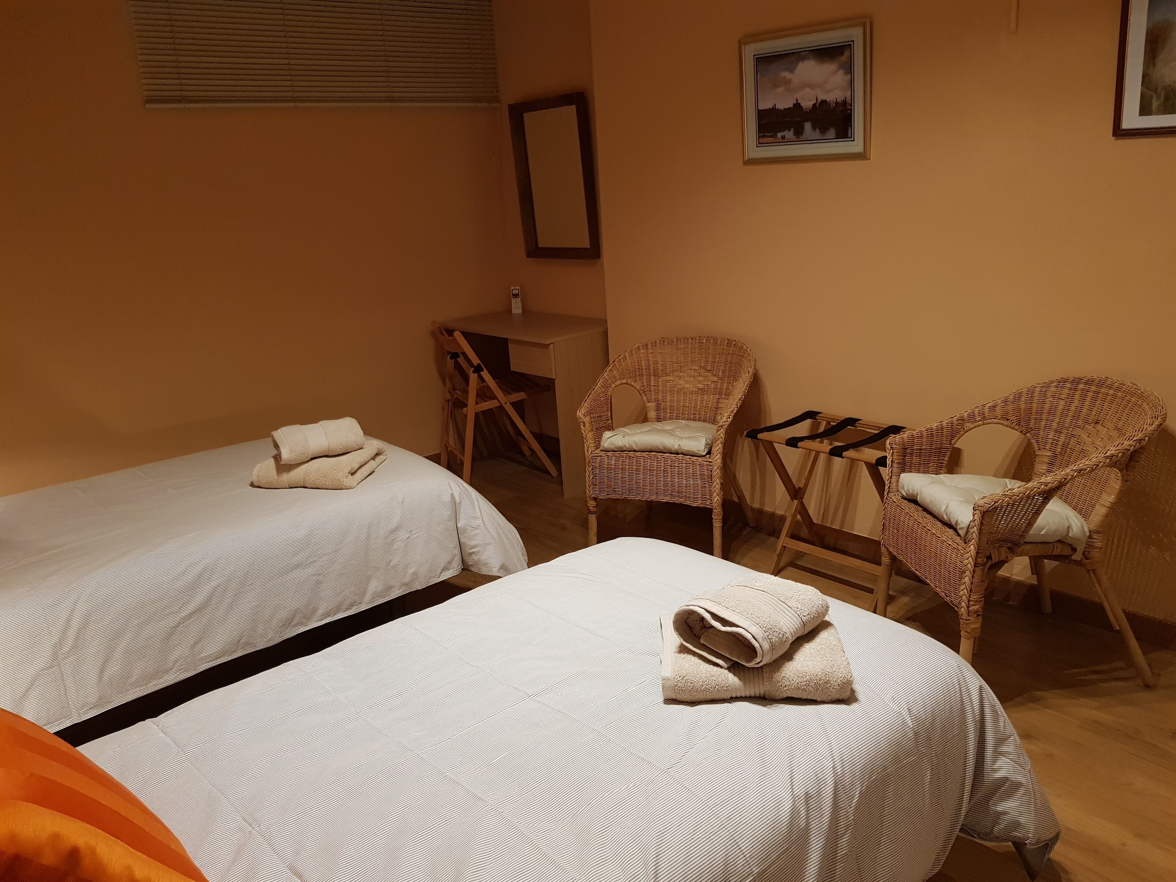 A room with two beds, a desk, and two wicker chairs.