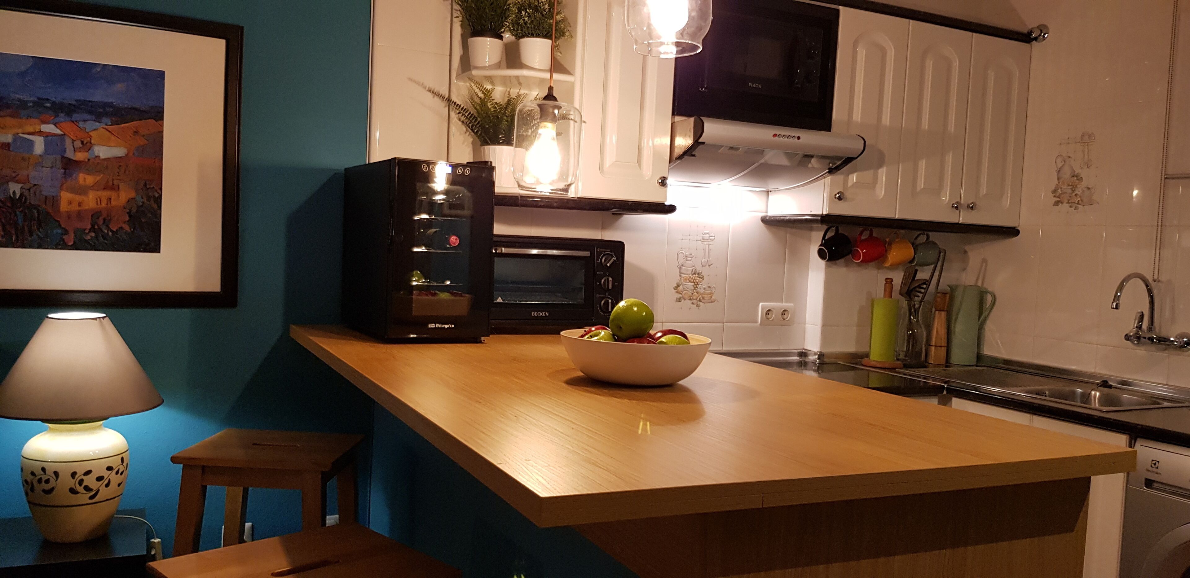 A kitchen with a wooden countertop, a black refrigerator, a microwave, a sink, and a bowl of fruit.