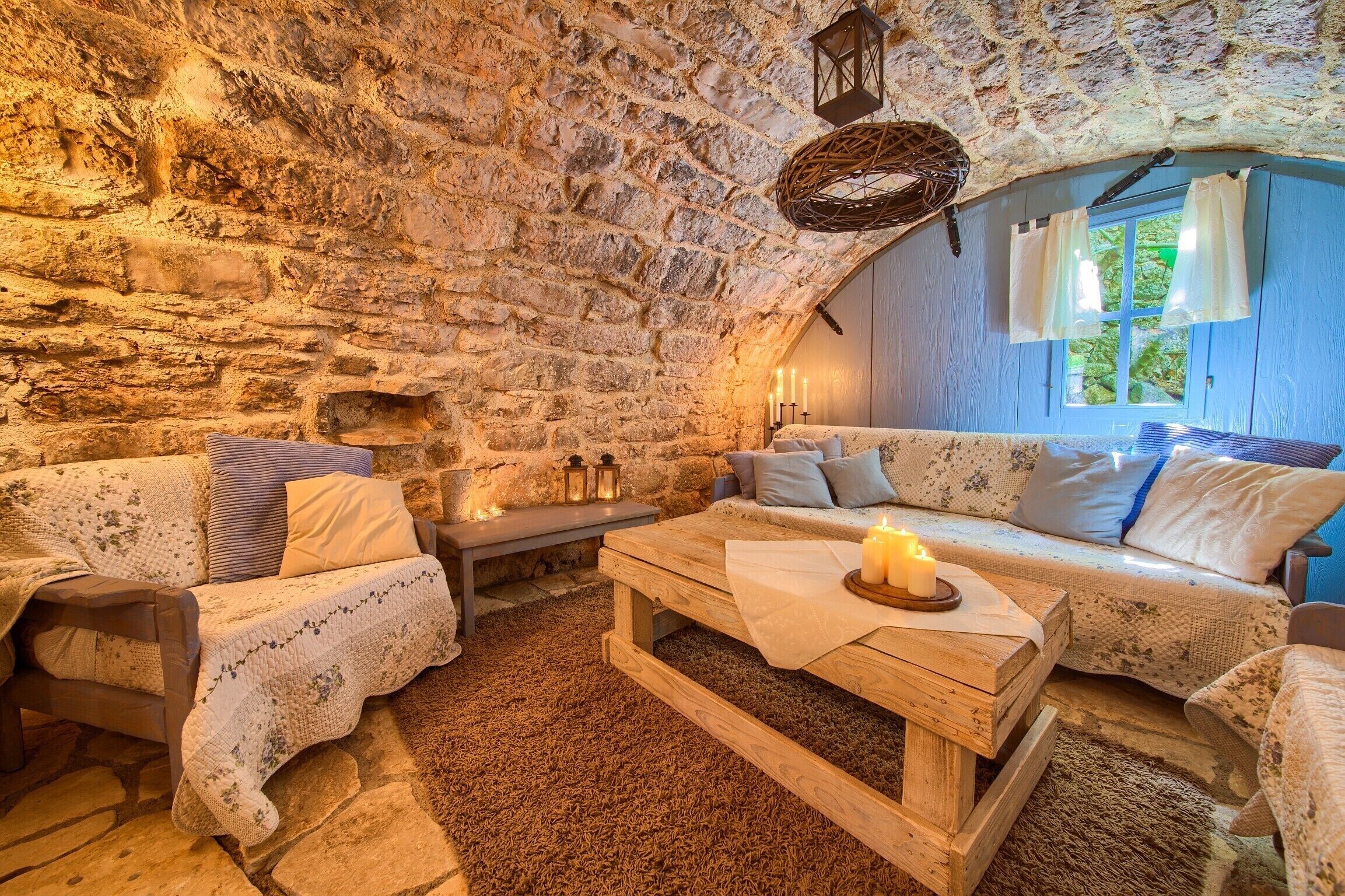 Una habitación acogedora y rústica con paredes de piedra, un banco de madera, un sofá y una ventana con cortinas.
