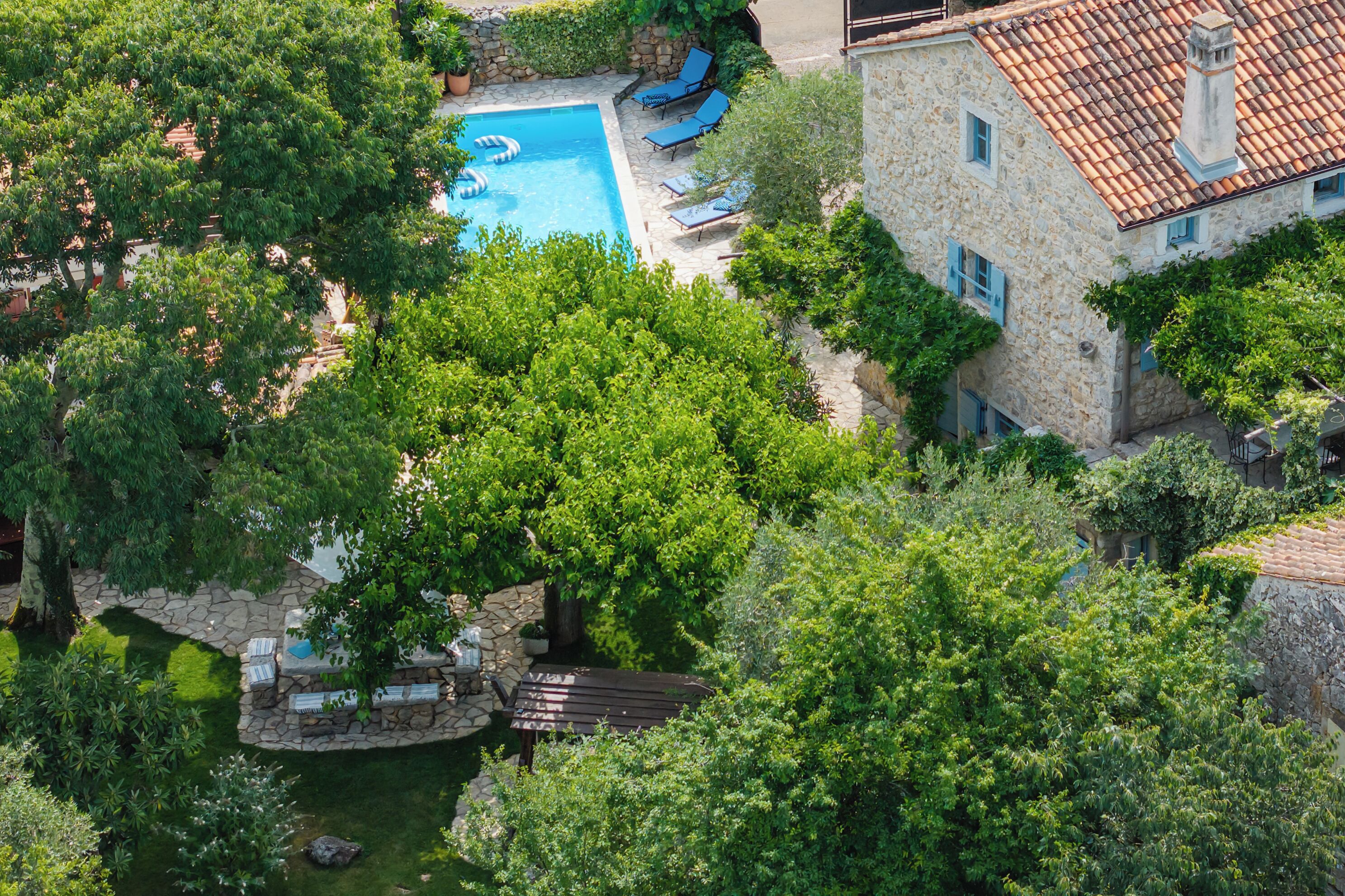 A stone building with a swimming pool, surrounded by lush greenery and trees.