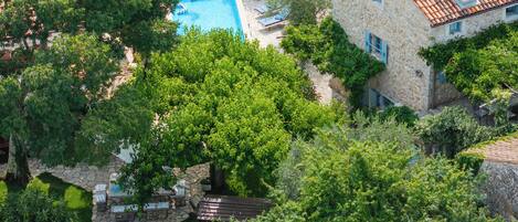 A stone building with a swimming pool, surrounded by lush greenery and trees.