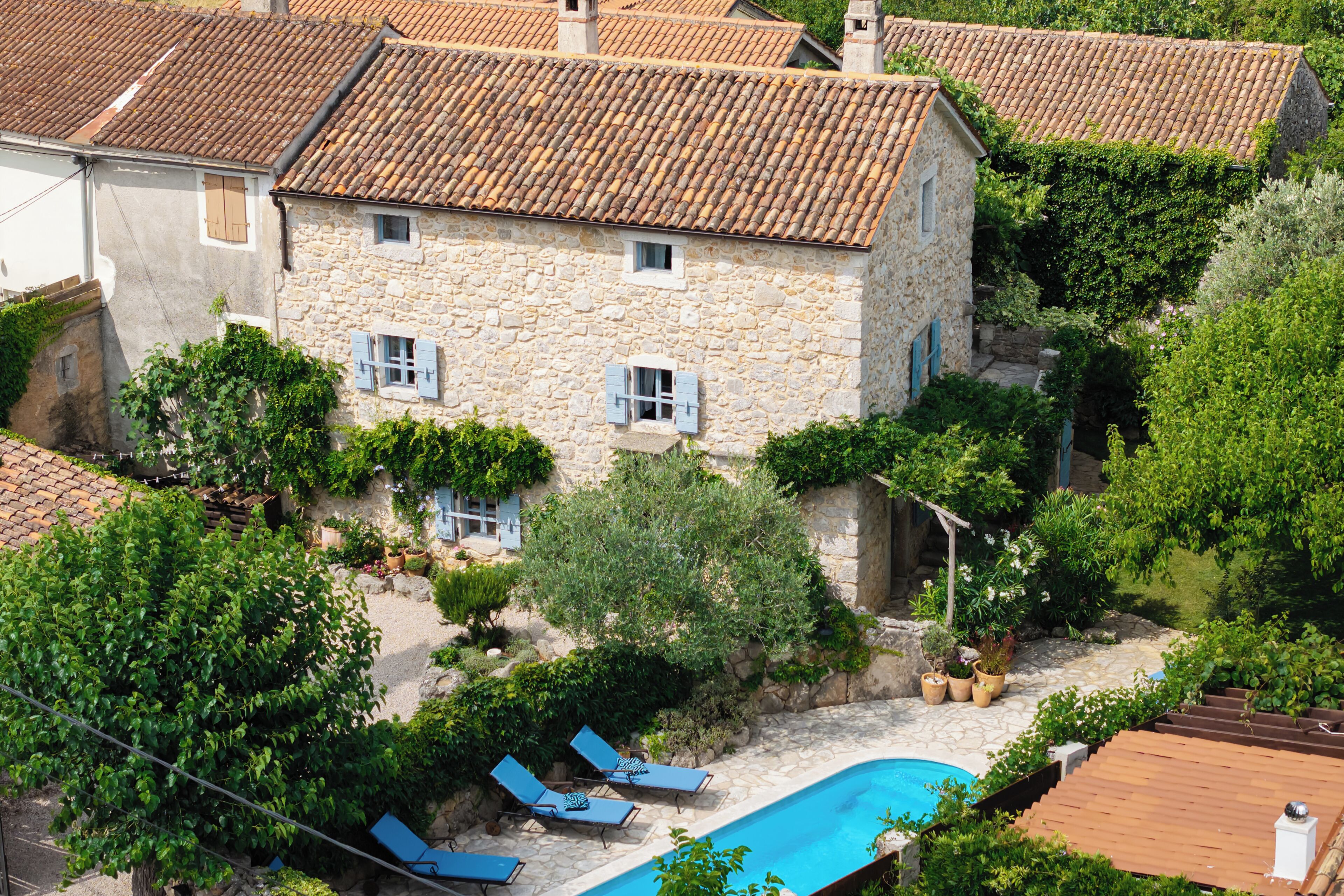A stone house with a swimming pool, blue shutters, and a garden.