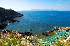 A coastal landscape with clear blue water, rocky shores, and a distant sailboat.