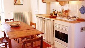 Een keuken met een houten tafel, stoelen, een fornuis en diverse keukengerei.