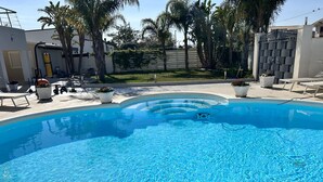 A clear blue pool with a curved edge, surrounded by potted plants and outdoor furniture. - Villa With Pool Near The Sea.Syracuse, Plemmirio, Arenella,Fontane Bianche  (Siracusa)