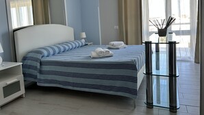 A hotel room with a bed, a nightstand, a lamp, a glass table with a vase, and a view of the outdoors. - Villa With Pool Near The Sea.Syracuse, Plemmirio, Arenella,Fontane Bianche  (Siracusa)
