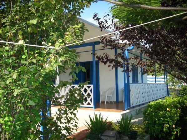 A covered outdoor seating area with a white fence and blue accents, surrounded by lush greenery.