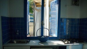 Una cocina con azulejos azules, una ventana con contraventanas, un lavamanos, una estufa y un lavavajillas.