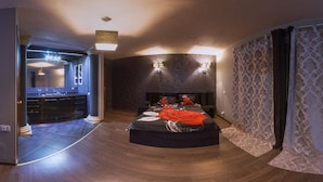 Quarto moderno com cama curva, um espelho grande e banheiro com toucador escuro.