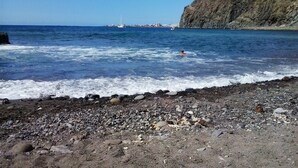 Uma praia rochosa com ondas quebrando na costa e uma pessoa nadando na água.