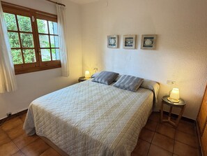 Une chambre à coucher avec un grand lit, deux tables de chevet avec des lampes, une fenêtre avec des rideaux et trois tableaux encadrés accrochés au mur.