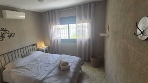 Een slaapkamer met een bed, een bedlamp, een wandheater, een raam met gordijnen en een haakje aan de muur.