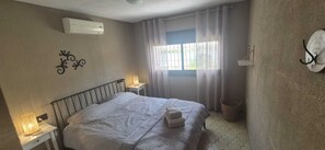 Un dormitorio con cama, lámpara de noche, calentador de pared, ventana con cortinas y un gancho en la pared.