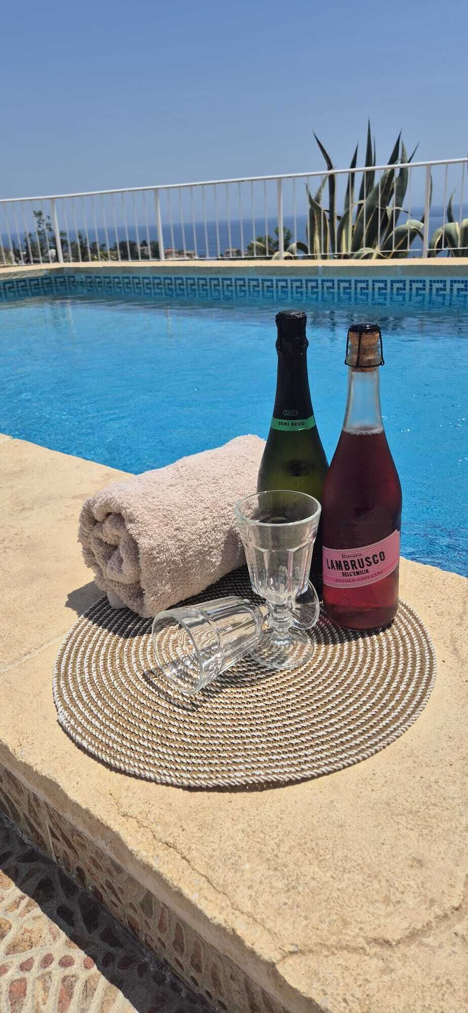 A poolside setting with a towel, a glass, and two bottles of wine.