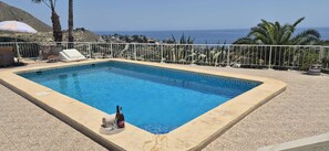 Una piscina rectangular con borde de azulejos, una botella de vino tinto y una copa junto a la piscina.