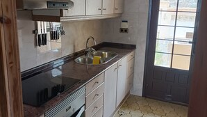Een keuken met lichte houten kastjes, een roestvrijstalen spoelbak en een betegelde vloer.