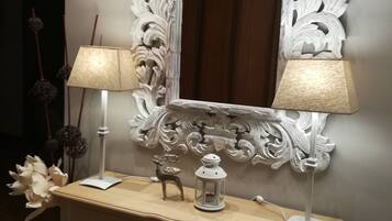 Un espejo blanco ornamentado con un marco decorativo, una consola de madera con cajones, dos lámparas, un pequeño ciervo decorativo y un farol.