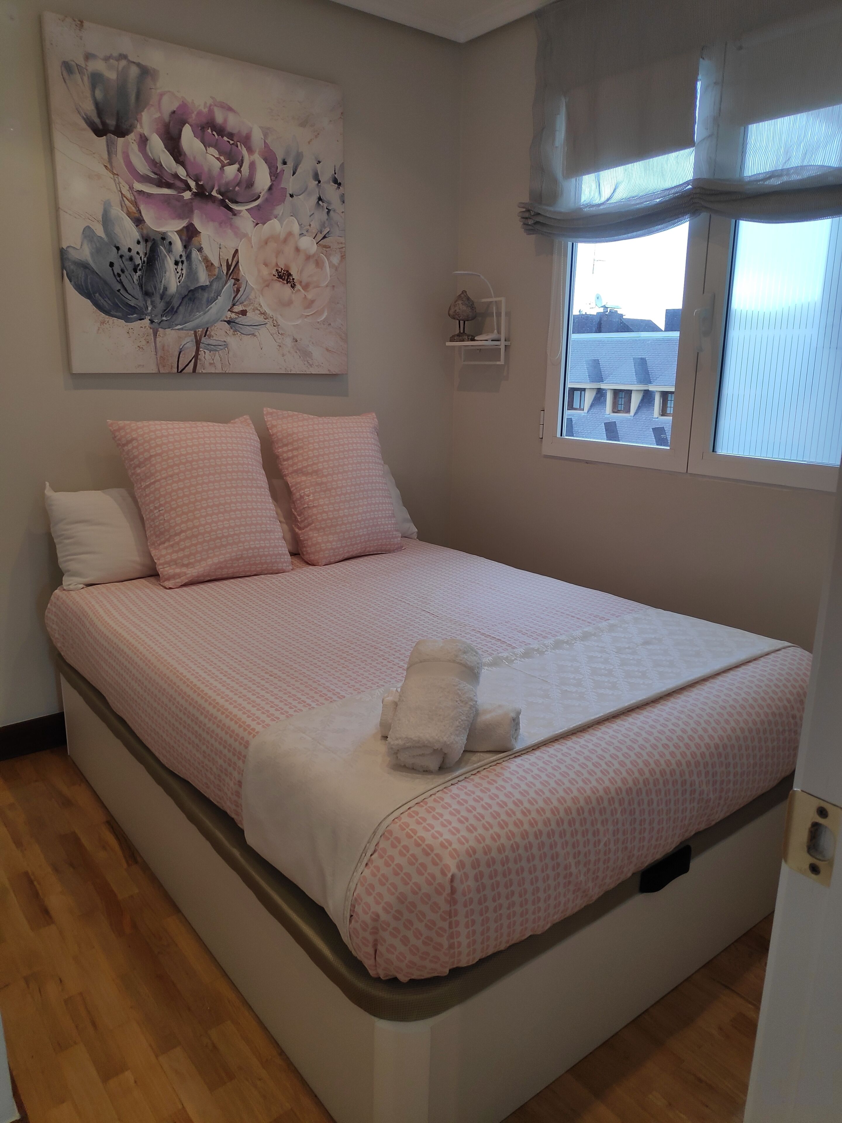 Une chambre à coucher avec un lit, des oreillers, un tableau, une fenêtre et une lampe.