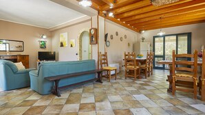 A living room with a blue sofa, wooden dining table, and chairs, a television, and a kitchen area with a refrigerator. - Villa with swimming pool a few km from the sea Selinunte (Partanna)