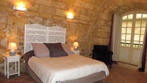 A bedroom with a stone wall, a bed with a white headboard, two bedside lamps, and a chair. - Great warm T2 68 M2, atypical, in the historic center (Bordeaux)