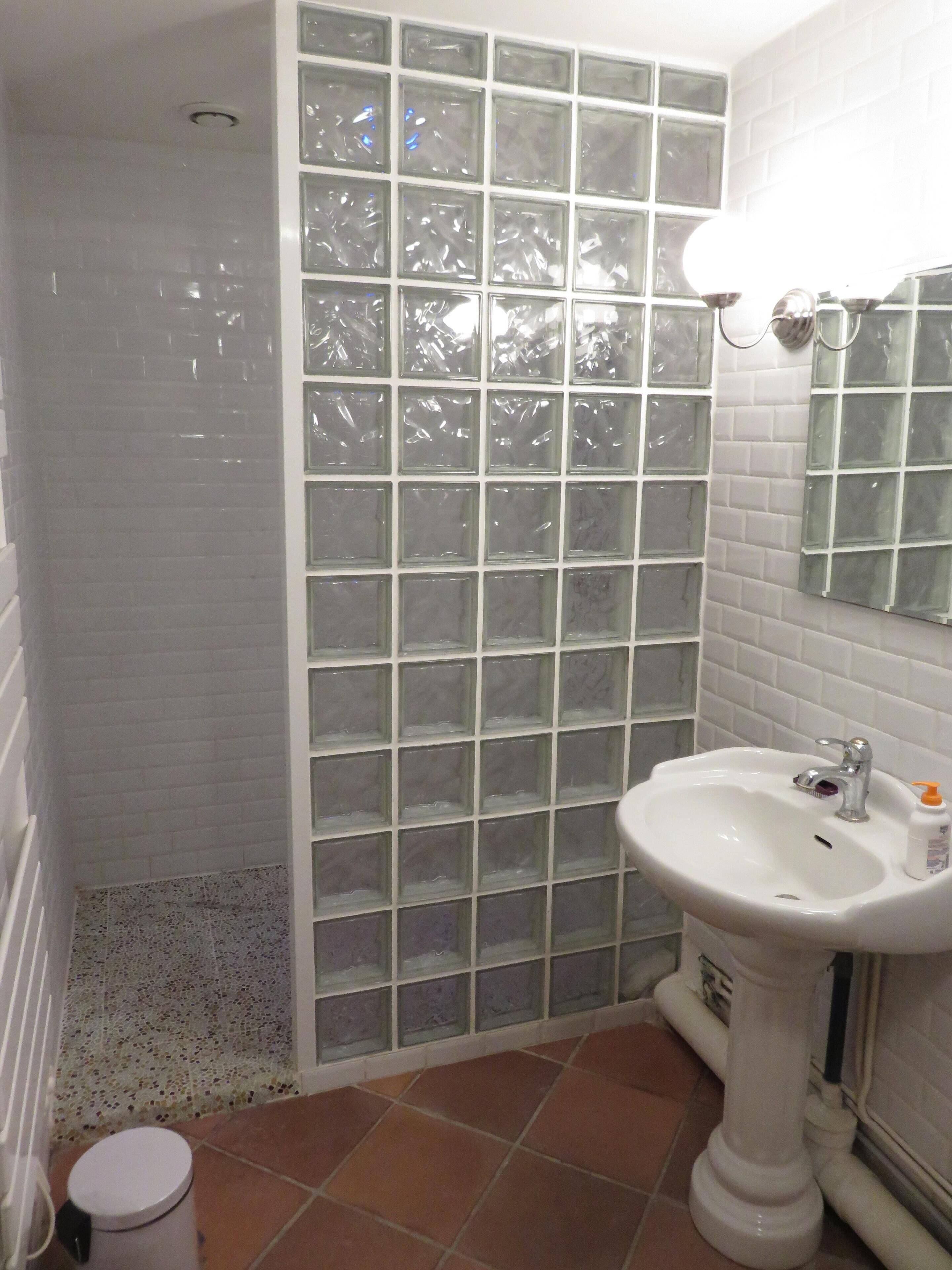 A bathroom with a glass shower enclosure, a white sink with a mirror, and tiled walls.